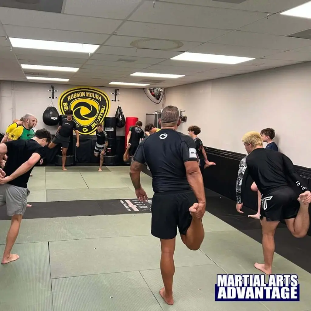 Martial arts students performing balance and leg stretches together during a group warm-up class to build confidence in martial arts.